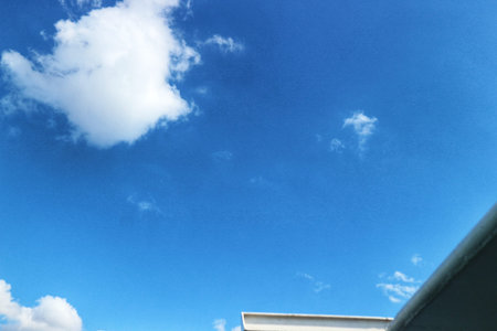 Bright blue sky features fluffy white clouds above a building's exterior creating a serene atmosphere suitable for backgrounds.のeditorial素材