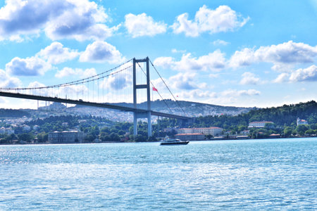 Istanbul, Turkey on 12 July 2022. Bosphorus. A long cable suspension bridge spans across the water, with a boat passing underneath, under a bright cloudy sky ideal for travel related content.のeditorial素材
