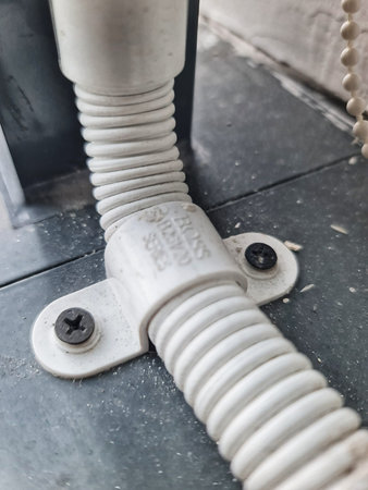 Jakarta, Indonesia on 26 September 2025. Corrugated white conduit is mounted with a bracket and screws to a gray surface, creating a utilitarian and functional visual, ideal for technical or industrial content.のeditorial素材