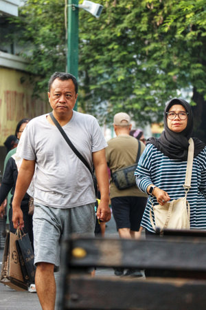 Yogyakarta, Indonesia on 22 Feb 2025. People walking with neutral expressions on a city street, wearing muted clothing and natural light creates an everyday scene suitable for urban lifestyle marketing.のeditorial素材