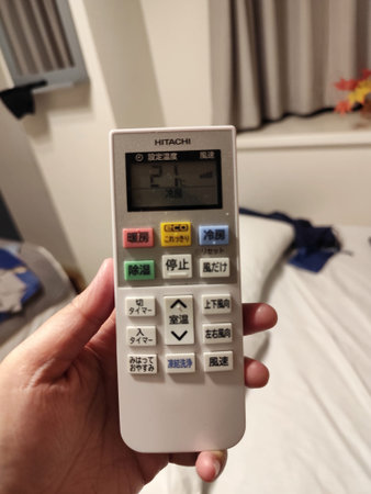 Tokyo, Japan on 13 Oct 2025. Hand holding a white remote control displaying settings with Japanese...