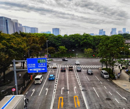 Tokyo, Japan on 13 Oct 2025. Elevated view shows a busy city street with multiple vehicles moving and pedestrians walking alongside, featuring green trees and modern buildings under a cloudy sky, suitable for urban planning or travel related projects.のeditorial素材