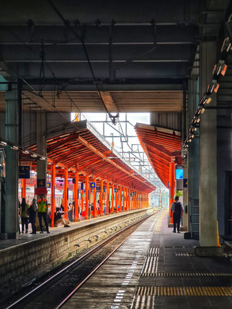 Bekasi, Indonesia on 27 Jun 2025. Passengers stand and wait on the train platform under an orange...