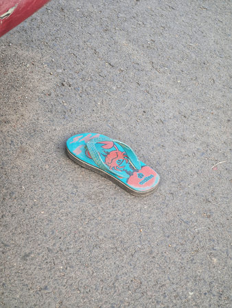 Semarang, Indonesia on 27 Jun 2025. Lone blue flip-flop with red design rests on gray textured...