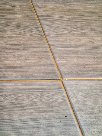 Close-up shot features grey, wood-look tiles arranged in a geometric pattern with tan grout,...