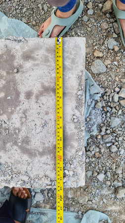 Cracked concrete surface is measured with a yellow tape measure by a person in sandals, shot from...