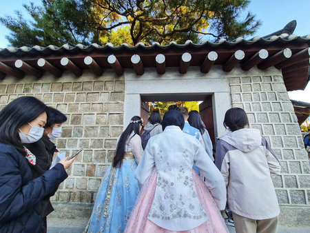 Seoul, South Korea on 10 Nov 2024. Gyeongbokgung. A group of people are entering through a stone gate, wearing traditional attire and face masks; great for historical sites or travel content.のeditorial素材