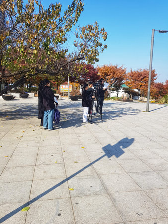 Seoul, South Korea on 12 Nov 2024. Film crew is working outdoors with camera and tripod under a bright blue sky with trees showing autumn colors, suitable for entertainment and media industry.のeditorial素材