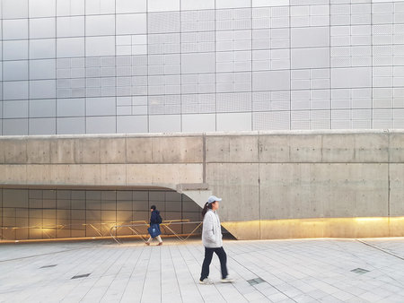 Seoul, South Korea on 7 Nov 2024. Woman is walking across a gray tiled square with unique concrete...