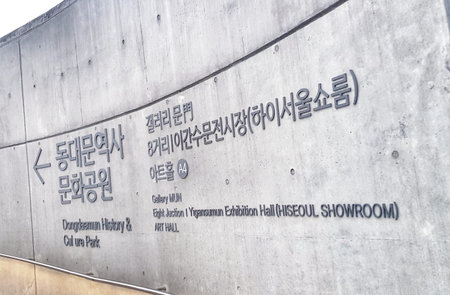 Seoul, South Korea on 7 Nov 2024. Rough gray concrete wall displaying black Korean and English inscriptions at Dongdaemun History & Culture Park, providing informative context for urban planning and architectural designs.のeditorial素材
