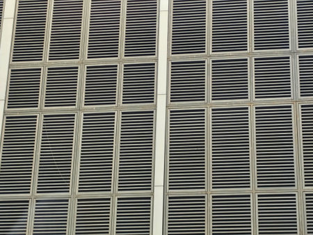 Close-up of a modern building facade featuring uniform ventilation grilles in neutral tones creating...