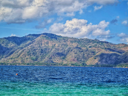 Scenic landscape featuring verdant hills meeting the tranquil ocean under a blue sky dotted with...