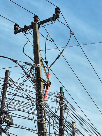 Utility pole is crowded with a web of black wires against a bright blue sky creating a visual...