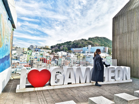 Busan, South Korea on 8 Nov 2024. Gamcheon. A woman in a coat relaxes on oversized letters with a...
