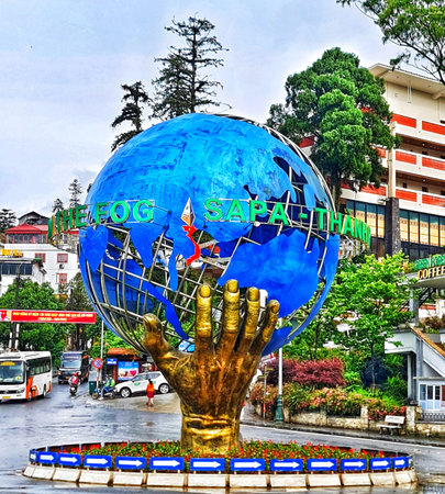 Sa Pa, Vietnam on 15 May 2025. Large sculpture of a blue globe held by a golden hand stands in a city center surrounded by traffic, buildings, and landscaping creating a vibrant travel and tourism atmosphere.のeditorial素材