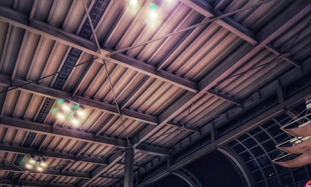 Interior view of a metal roof framework with beams and hanging lights creating an industrial...