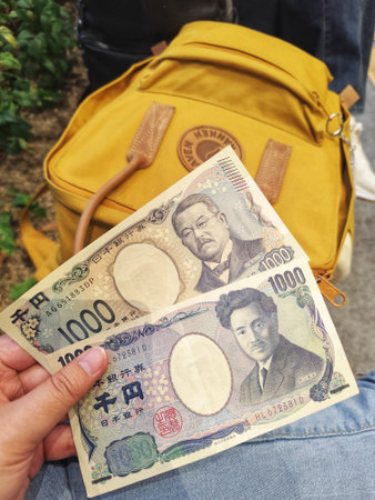 Osaka, Japan on 18 Oct 2025. Close-up of a hand holding two 1000 yen notes in front of a yellow...