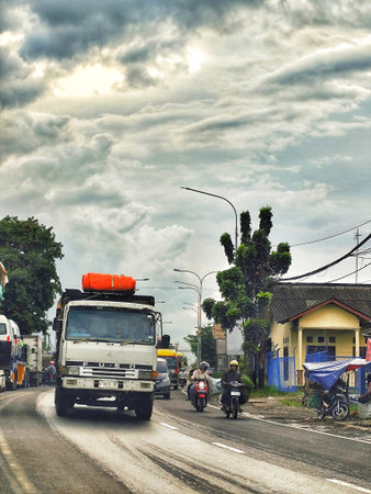 Cikampek, Indonesia on 9 Jan 2026. A white Fuso truck navigates a wet road while motorcycles and...