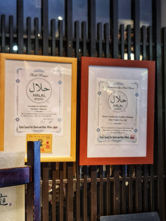 Kyoto, Japan on 17 Oct 2025. Two framed halal certificates mounted on a dark wooden slatted wall with soft indoor lighting and a colorful wooden railing in the foreground.