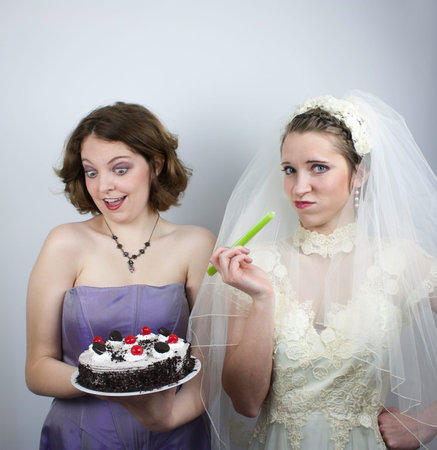 A bridesmaid holds a cake and tries to tempt a bride that is eating a piece of celery の写真素材