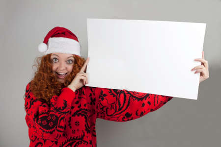 Pretty young woman wearing Santa hat and holding blank signの写真素材
