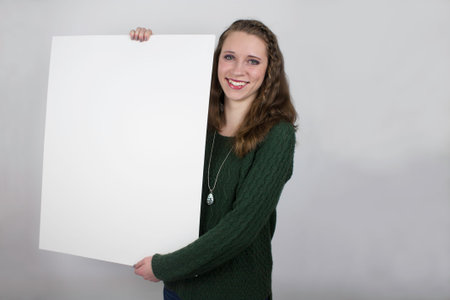 Pretty young woman wearing green sweater holding blank sign