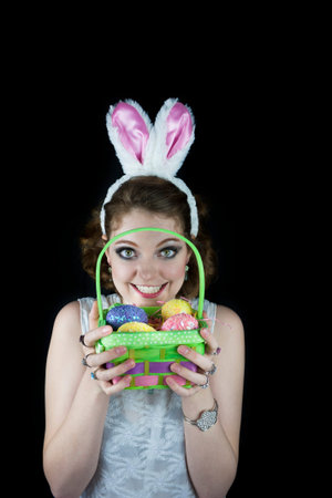 Young woman posing with rabbit ears and Easter basket with sequin eggs on black background 