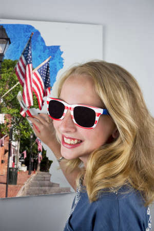 Pretty young blond girl painting flags and wearing 4th of July sunglassesの写真素材