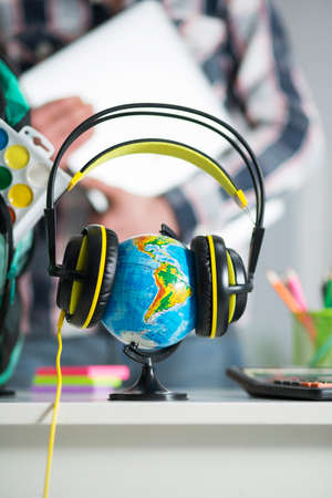 Earth globe is on the table in headphones. Interior of the apartment. A guy with a laptop in hand on the backgroundの写真素材