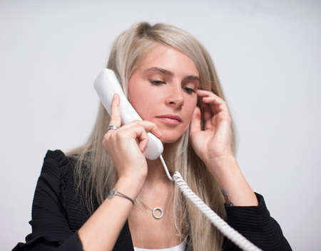 Beautiful blonde thoughtful businesswoman talk phone in office portrait.の写真素材