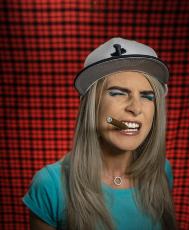 A sexy smoking beautiful hipster woman in a white cap and a turquoise T-shirt with a cigar. Evil...
