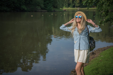 Beautiful young woman in hat and sunglasses resting on the lake in the summer outdoors. The concept of street fashionの写真素材