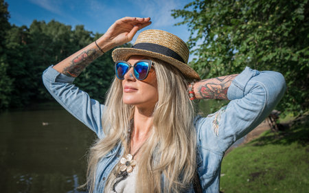 Beautiful young woman in hat and sunglasses resting on the lake in the summer outdoors. The concept of street fashionの写真素材
