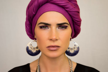 A beautiful European woman in a bright pink turban with large oriental earrings. The style of urban...