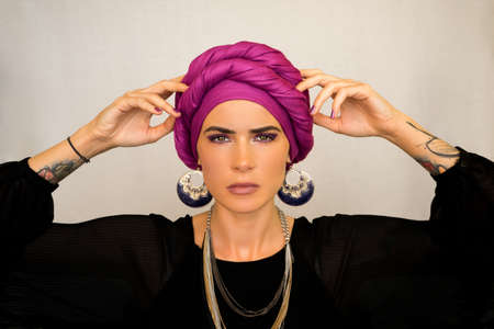 A beautiful European woman in a bright pink turban with large oriental earrings. The style of urban fashion.の写真素材