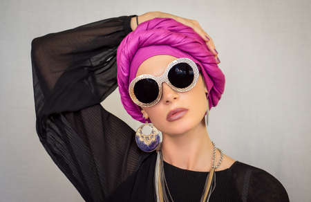 A beautiful European woman in a bright pink turban with large oriental earrings, in large round glasses looks at the camera. The style of urban fashion.の写真素材