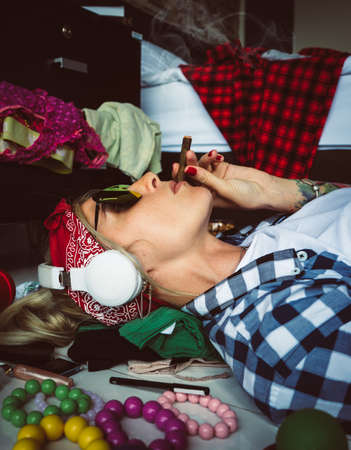 after studying blonde student, lying on the floor in headphones and sunglasses, listening to music and smoking a cigarette. The image of a modern student, education, Accessories of a modern young girlの写真素材