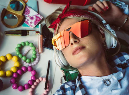 Closeup portrait of blonde with headphones and sunglasses, rests on the floor listening to music. The mess in the room. Modern womens styleの写真素材