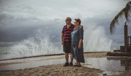 An elderly couple stands on the beach and watching as the approaching storm into the waves.の写真素材