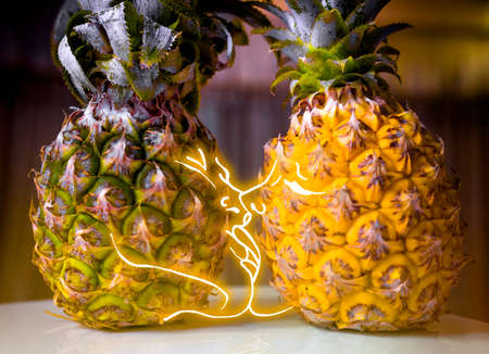 Pineapple lovers couple kissing in an intimate light. A boy and a girl. The concept of a tropical vacation.の写真素材