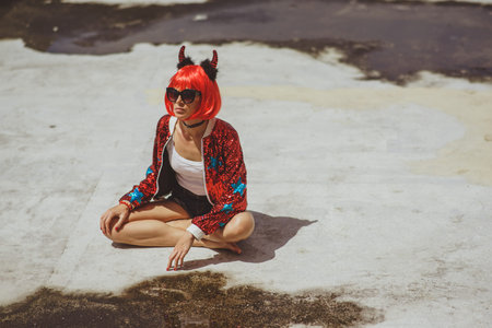 Beautiful girl devil sitting on city background near the puddle with his reflection. In anticipation...