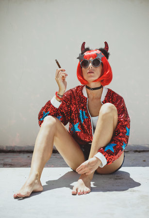 Beautiful girl devil sitting on white background and smoke cigar. In anticipation of Halloween....