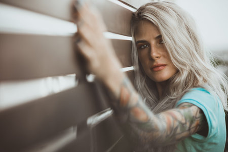 Portrait of a beautiful blonde closeup. Wearing a turquoise t-shirt. Arms tattooed. The concept of...
