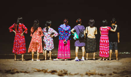 Chinese tourists stand with their backs to the camera, near the night sea in Thailand. Colorful clothes.の写真素材