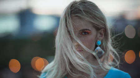 Portrait of beautiful young blonde in the turquoise shirt on the background of night city lights. Modern styleの写真素材