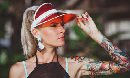 The girl in the red visor looking into the distance. Arms tattooed. Modern beach-ready look.の写真素材
