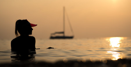 Silhouette of a beautiful girl bathing in the sea on her yacht in the rays of the setting sun. Holiday in Thailandの写真素材