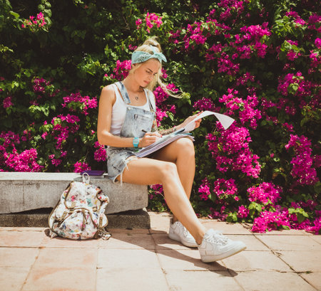 Girl student sitting in summer park and doing homework. Modern style of the girl. Model with tattoos