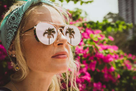 Close-up portrait of a young beautiful girl in glasses with reflection of tropical palms. Summer rest. Modern touristの写真素材
