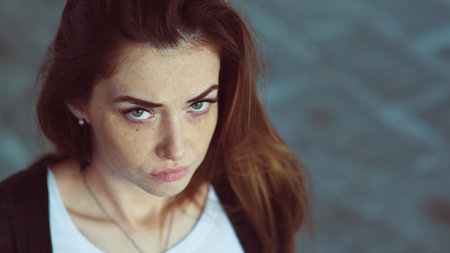Closeup portrait. Red-haired girl with a serious facial expression looking at the camera